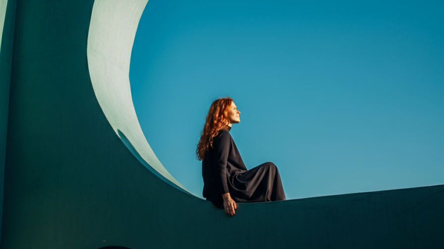 Person sitting on a modern architectural structure against a clear blue sky